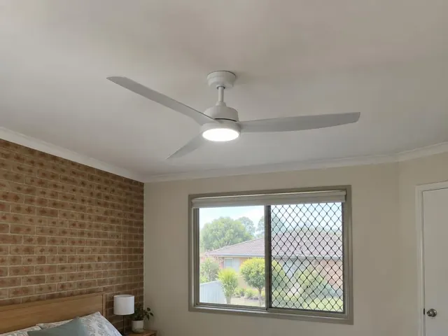 Ceiling fan with light on a bedroom ceiling above a bed, with brick feature wall and window in Berkeley Vale