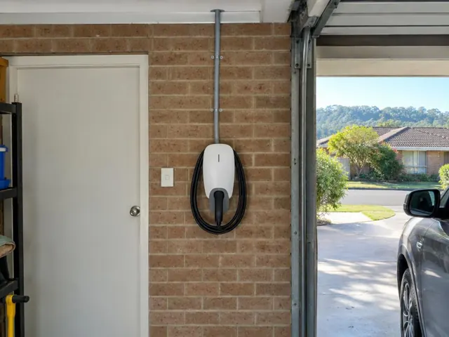 Wall-mounted EV charger on a brick garage wall beside a white door in Tumbi Umbi